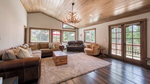 A spacious living room with a high ceiling, large windows, and a fireplace.