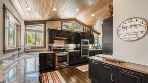 A modern kitchen with dark cabinetry, stainless steel appliances, and a large window providing natural light.