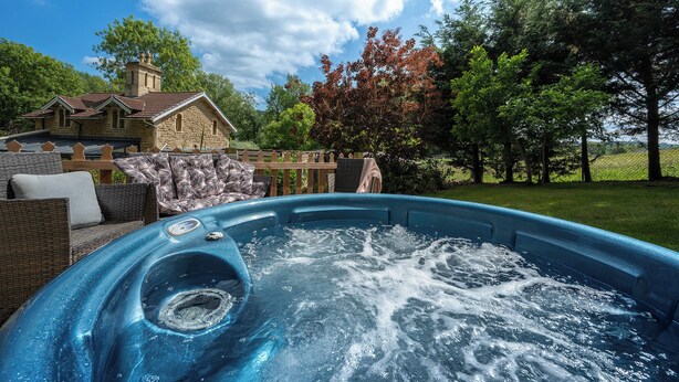 A hot tub in a backyard with a stone house, wicker furniture, and trees. - Lavender Lodge  (Bath)