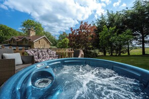 A hot tub in a backyard with a stone house, wicker furniture, and trees. - Lavender Lodge  (Bath)