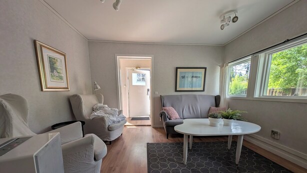 Een moderne woonkamer met een grijze bank, een witte fauteuil, een ronde salontafel en een kamerkleed met een patroon.