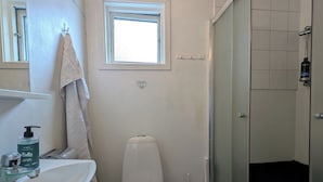 Een badkamer met een witte wastafel, toilet en douche. Boven het toilet bevindt zich een raam en er hangt een handdoek aan de muur.