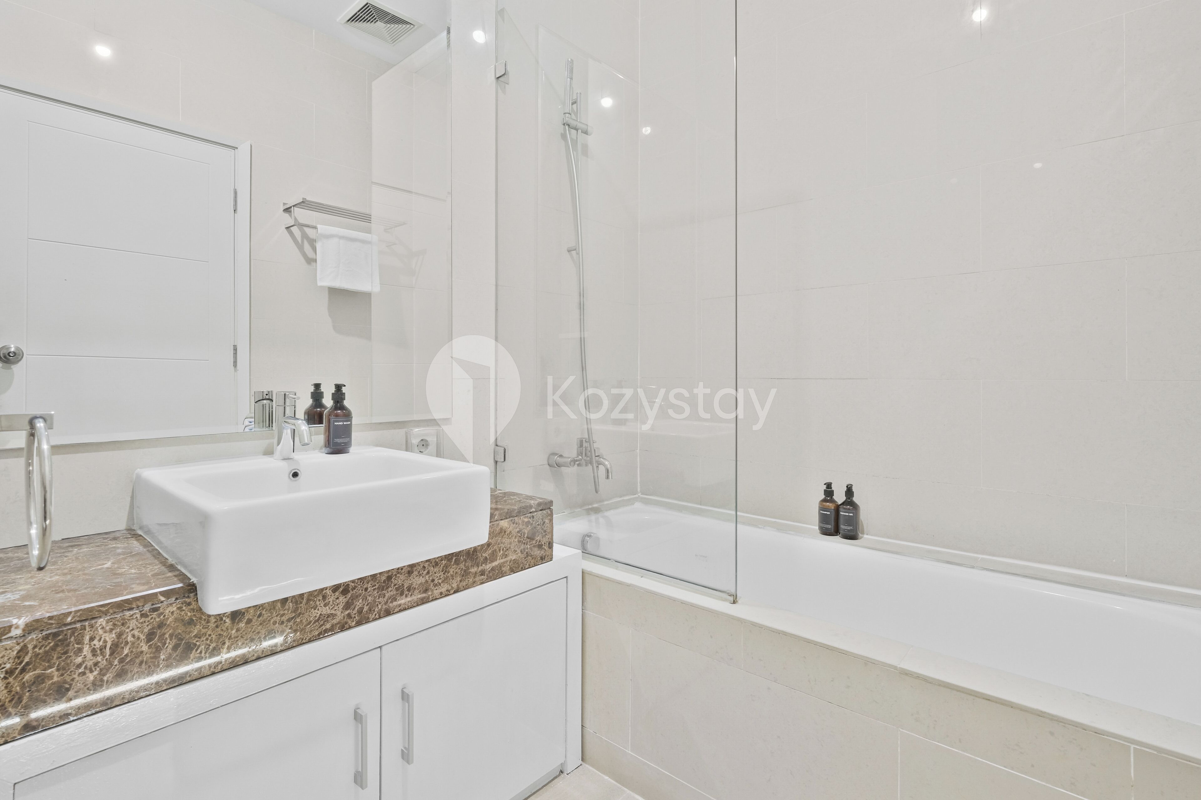 A modern bathroom with a white sink, marble countertop, and a glass-enclosed shower.