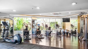 Ein modernes Fitnessstudio mit verschiedenen Cardiogeräten, Spiegelwänden und Blick auf Grünflächen.