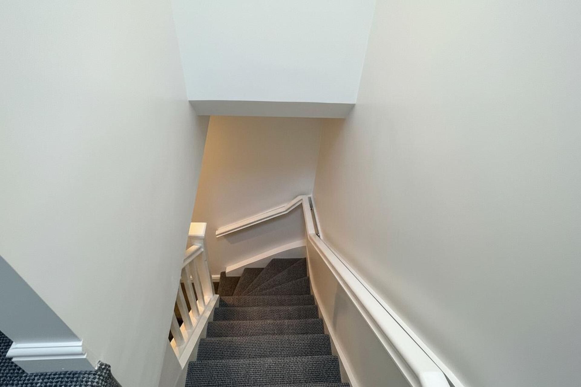 Una escalera estrecha con suelo alfombrado y paredes blancas.