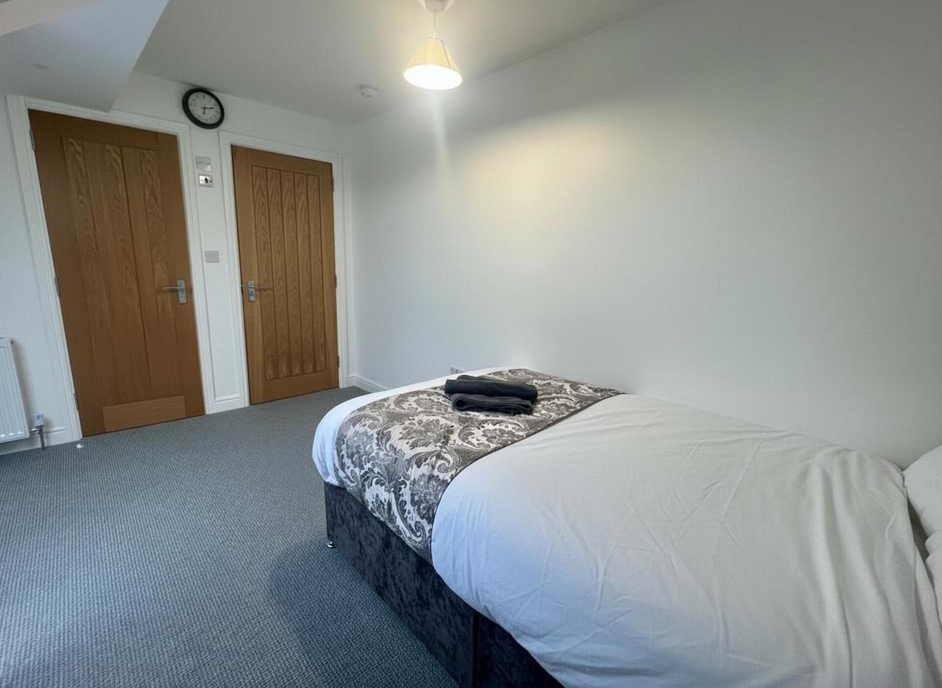 A bedroom with a bed, two wooden doors, a radiator, and a ceiling light.