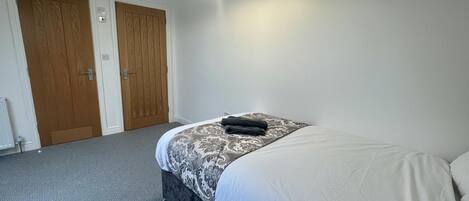 A bedroom with a bed, two wooden doors, a radiator, and a ceiling light.