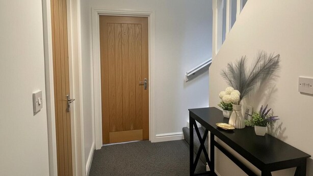 A hallway with a wooden door, a black console table with decorative items, and a carpeted floor. - Construction Crew Quarters:5brfree Wifi & Parking (Newcastle-upon-Tyne)