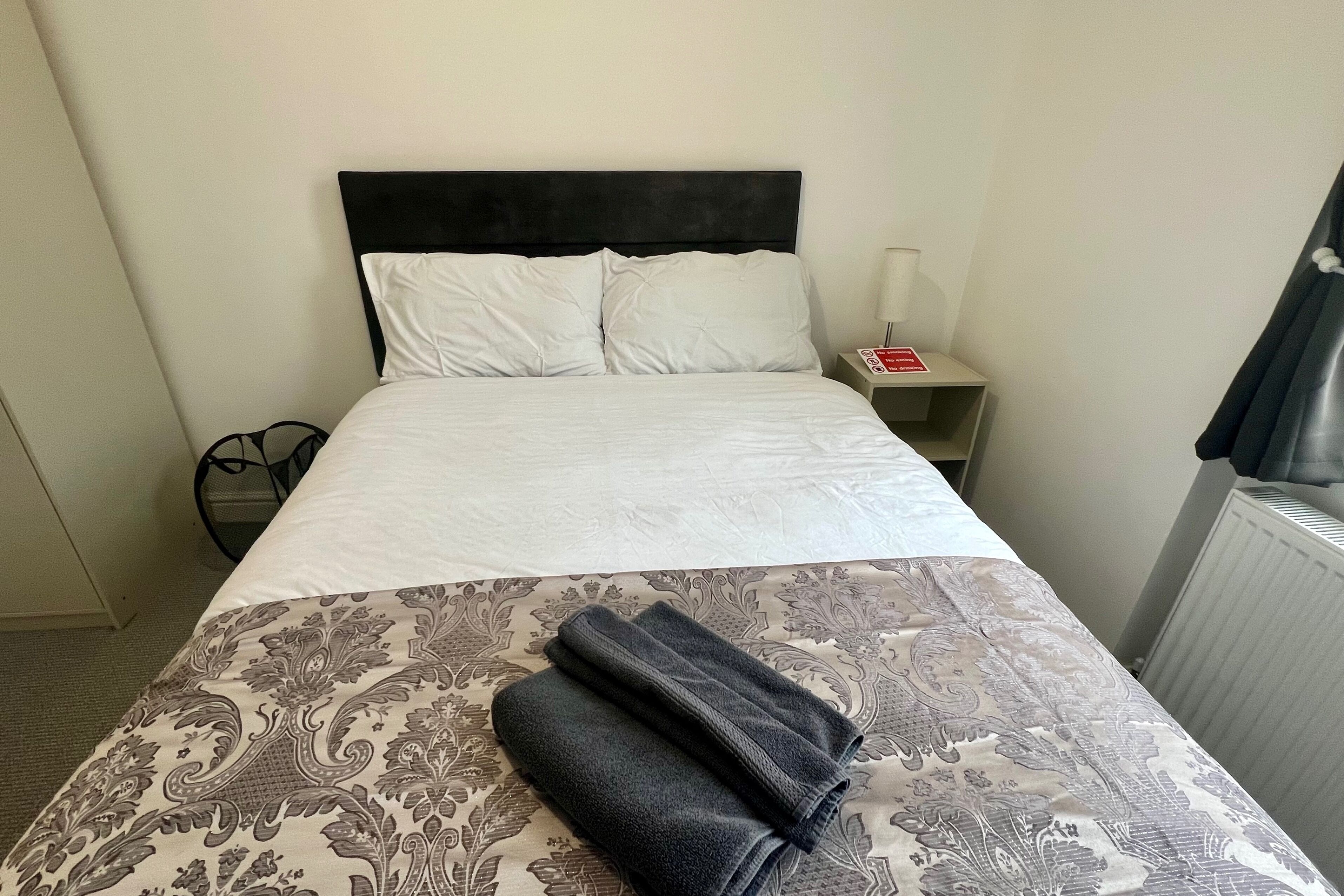 A neatly made bed with white linens and a patterned bedspread. There is a folded towel on the bedspread.