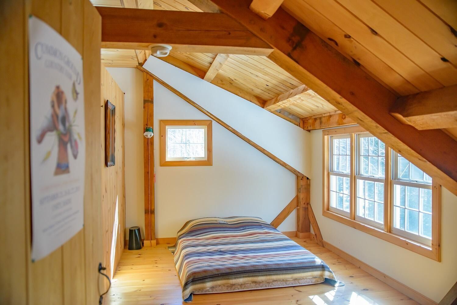 A small, cozy attic bedroom with a sloped ceiling, a single bed, a window, and a wooden floor.