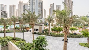 A modern hotel courtyard with palm trees, a pool, and high-rise buildings in the background.