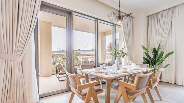 A dining area with a wooden table set for four, surrounded by chairs, with a large sliding glass door leading to an outdoor balcony.