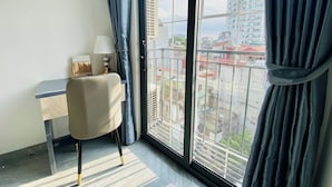 A room with a desk, chair, and a view of a cityscape through a large window. - Lilo's Homestay (Hanoi)