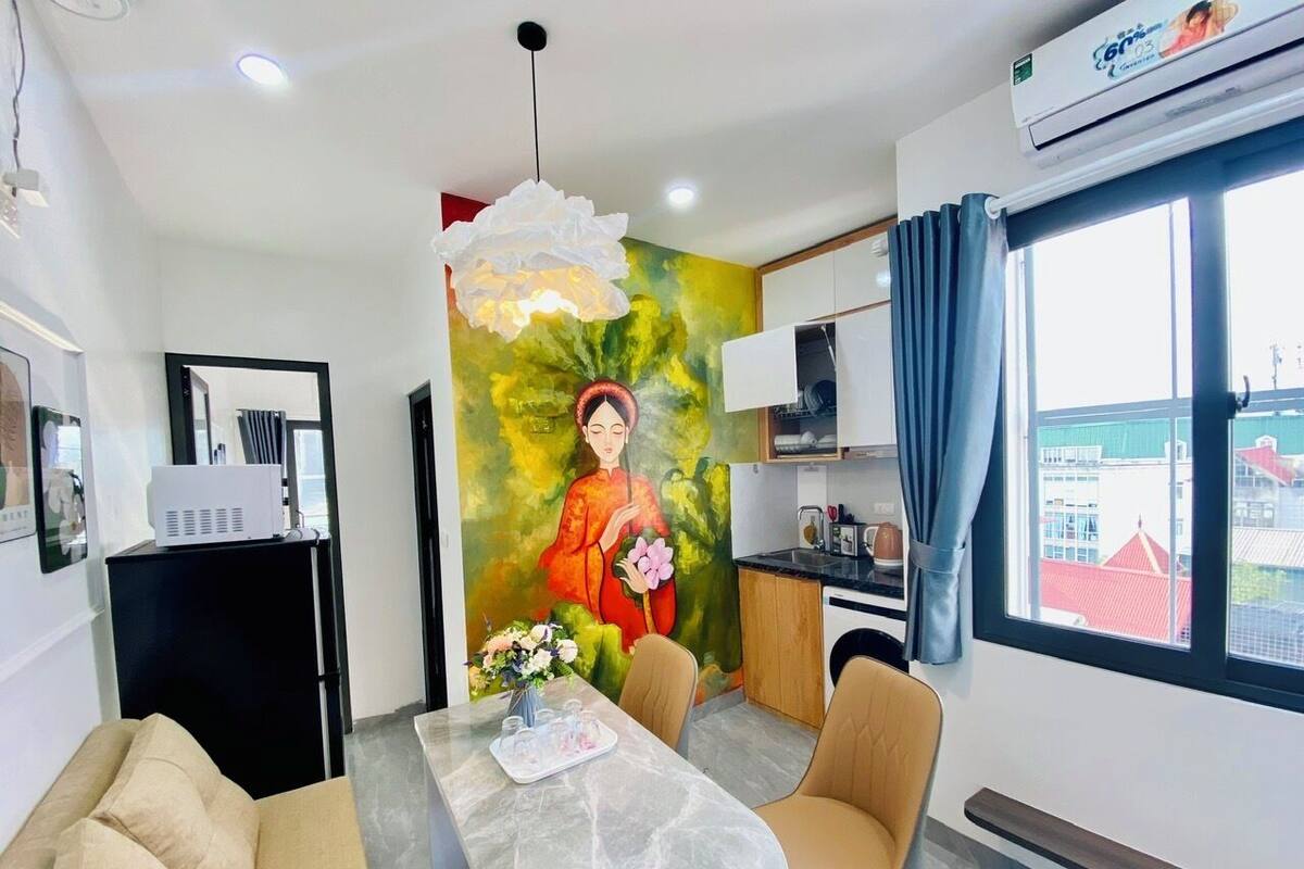 Une chambre d’hôtel moderne dotée d’un coin repas, d’une kitchenette, d’une grande fenêtre offrant une vue agréable et d’une fresque murale originale.