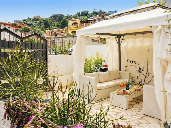 A covered outdoor seating area with a sofa and a table set with food and drinks.