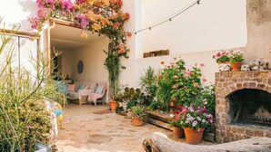 En gårdsplads med flisebelagte sten, en træbænk, en stenpejs og et udvalg af krukker med planter og blomster.