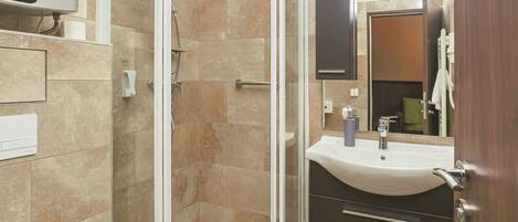 Un baño moderno con ducha de vidrio, inodoro blanco y tocador oscuro con lavamanos.