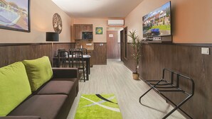 A hotel room with a sofa, a dining table with chairs, a kitchen area, and a TV mounted on the wall. - Park Hotel Bükfürdő (Bükfürdo)