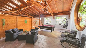 A spacious indoor area with a pool table, wicker furniture, and a hanging chair. - Park Hotel Bükfürdő (Bükfürdo)