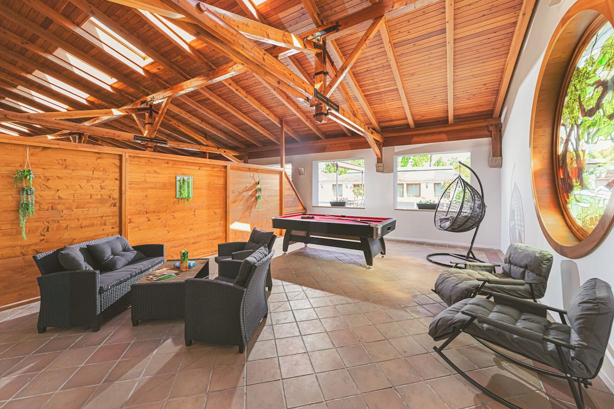 Un grand espace intérieur aménagé avec un billard, des meubles en osier et un fauteuil suspendu.