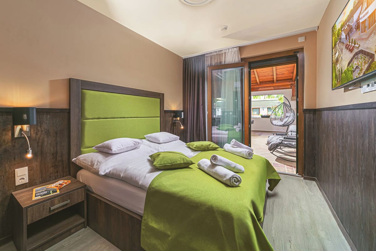 Une chambre d’hôtel comprenant un lit, une table de chevet, une fenêtre avec des rideaux, une vue sur l’extérieur et une porte donnant sur un balcon.