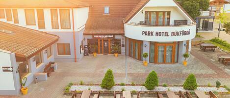A hotel with a central courtyard, outdoor seating, and a sign reading "Park Hotel Bükfürdö".