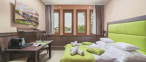 A hotel room with a bed, a desk, a chair, a coffee machine, and a painting on the wall.