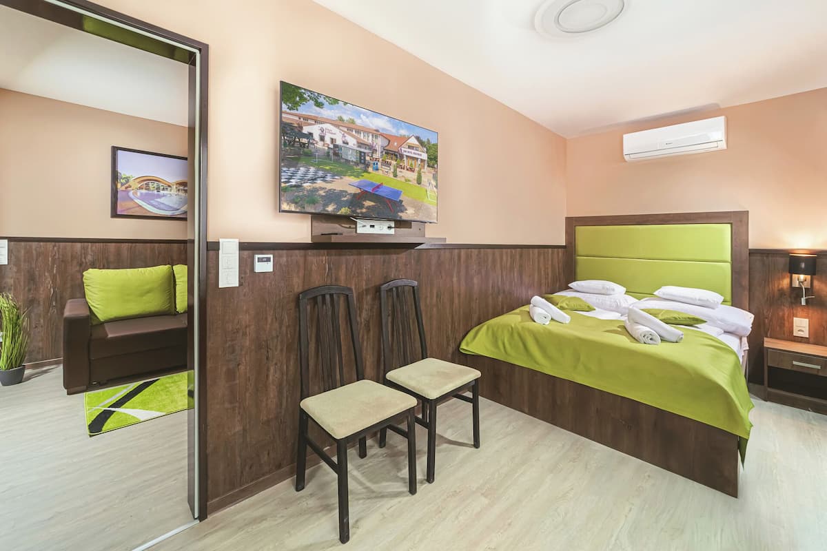 Une chambre d’hôtel avec un lit, deux chaises, une télévision et un tableau au mur.