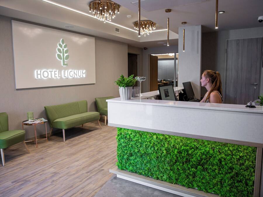 A hotel reception area with a modern design, including a reception desk, green seating, and a green wall feature.