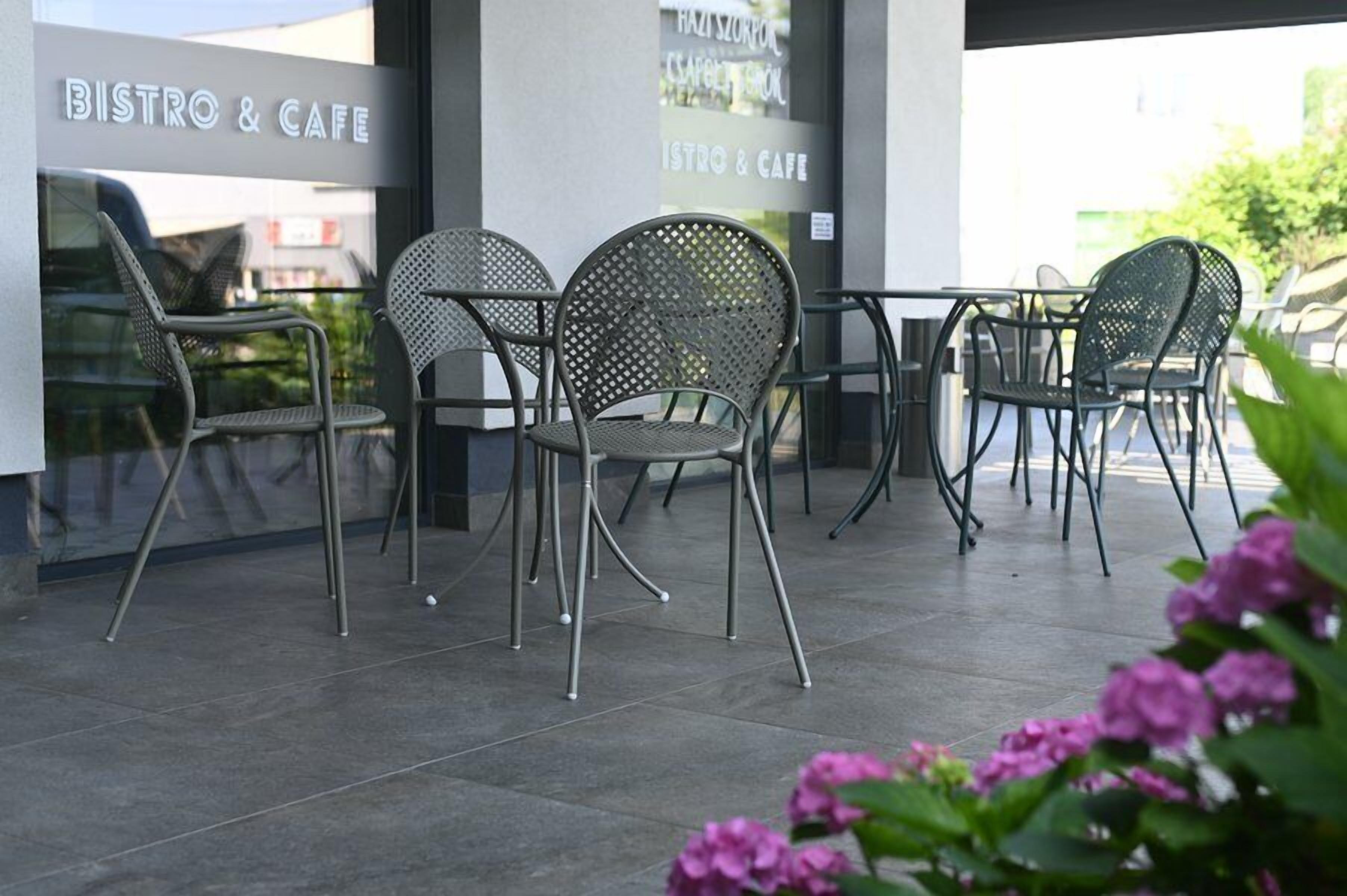 Un espace extérieur aménagé avec des chaises et des tables en métal, un sol carrelé et une enseigne indiquant « BISTROT ET CAFÉ ».