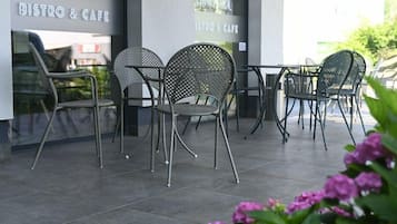 Un espace extérieur aménagé avec des chaises et des tables en métal, un sol carrelé et une enseigne indiquant « BISTROT ET CAFÉ ».