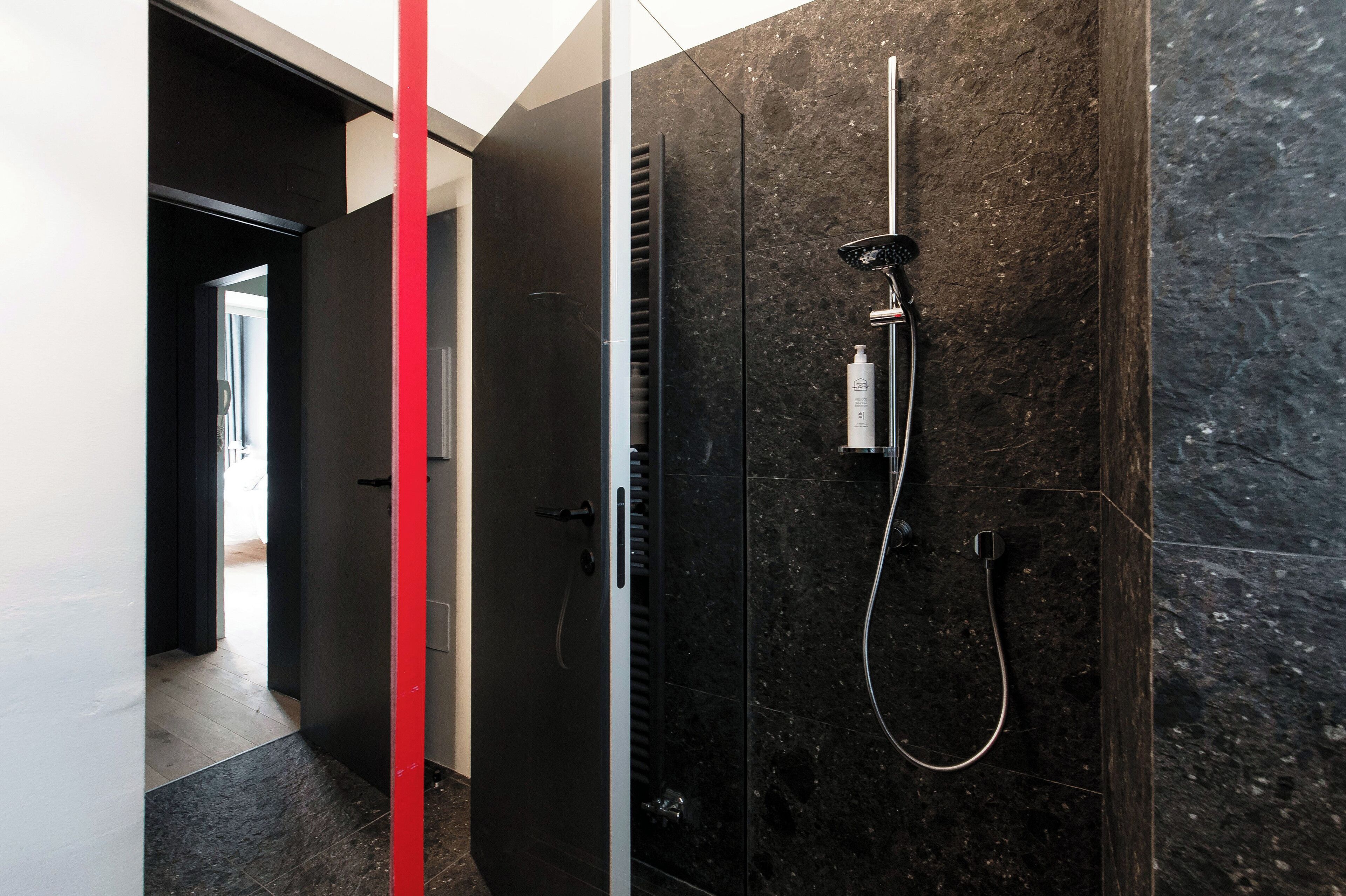A modern bathroom with a shower, a glass enclosure, and a red accent wall.