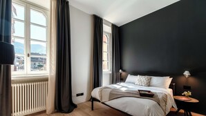 Un dormitorio moderno con una cama grande, una mesita de noche pequeña, un radiador y una ventana con cortinas.