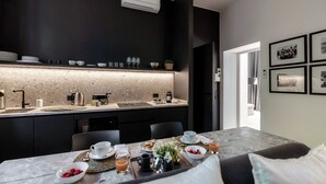 Una cocina moderna con protector contra salpicaduras oscuro, una encimera con diversos utensilios de cocina y una zona de comedor con desayuno servido.