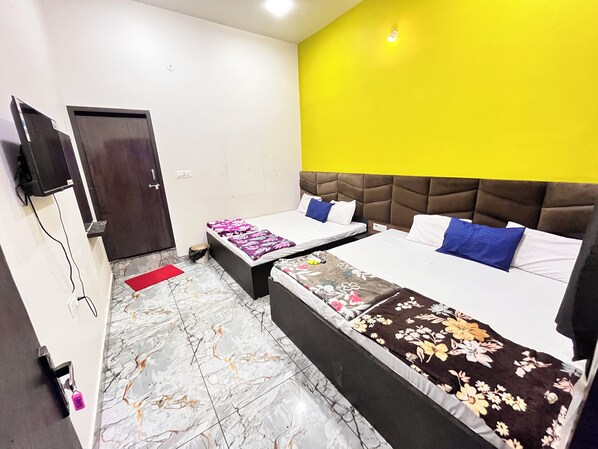 A hotel room with two beds, a television, a door, and a yellow accent wall.