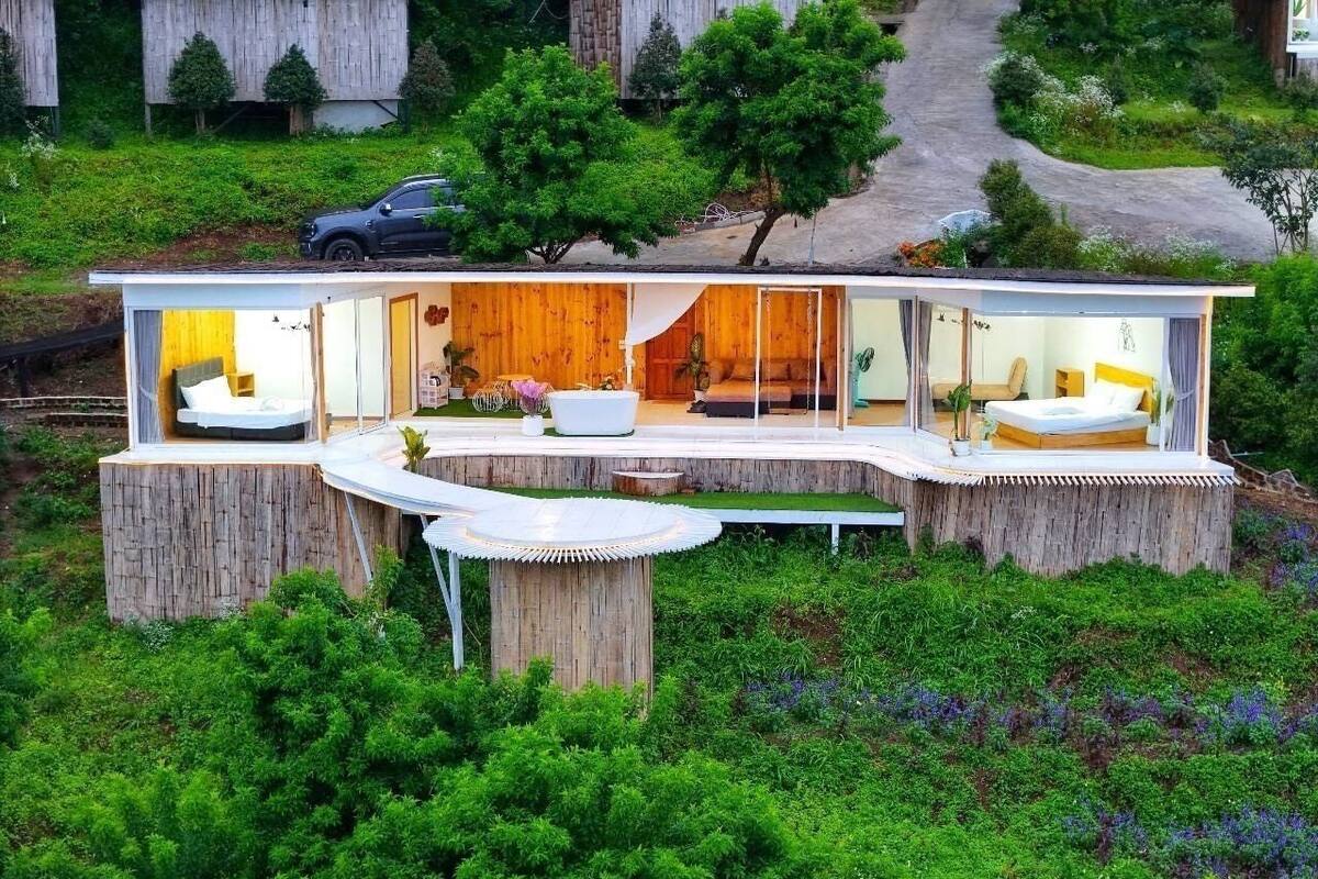Una casa moderna de planta oberta amb una zona d'estar central, dos dormitoris i una petita zona de seients a l'exterior.