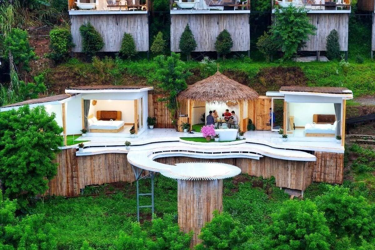 Un complex turístic modern amb allotjaments tipo cabana d'arbòria, una zona comuna central i vegetació abundant.