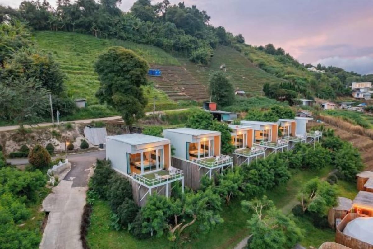 A hillside with modern, compact cabins featuring balconies and a lush, green environment.