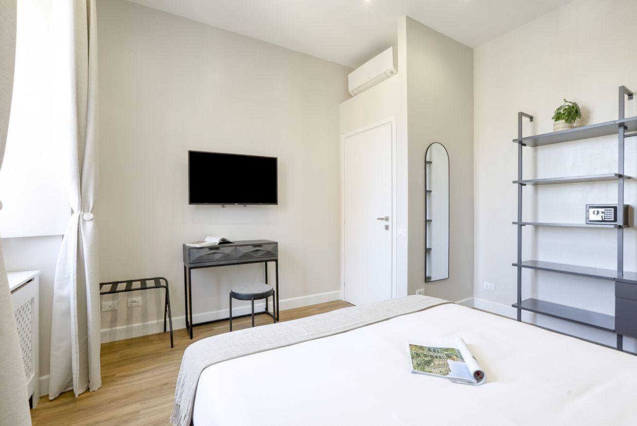 Une chambre à coucher comprenant un lit, un bureau, une chaise, un téléviseur, un miroir et une étagère.