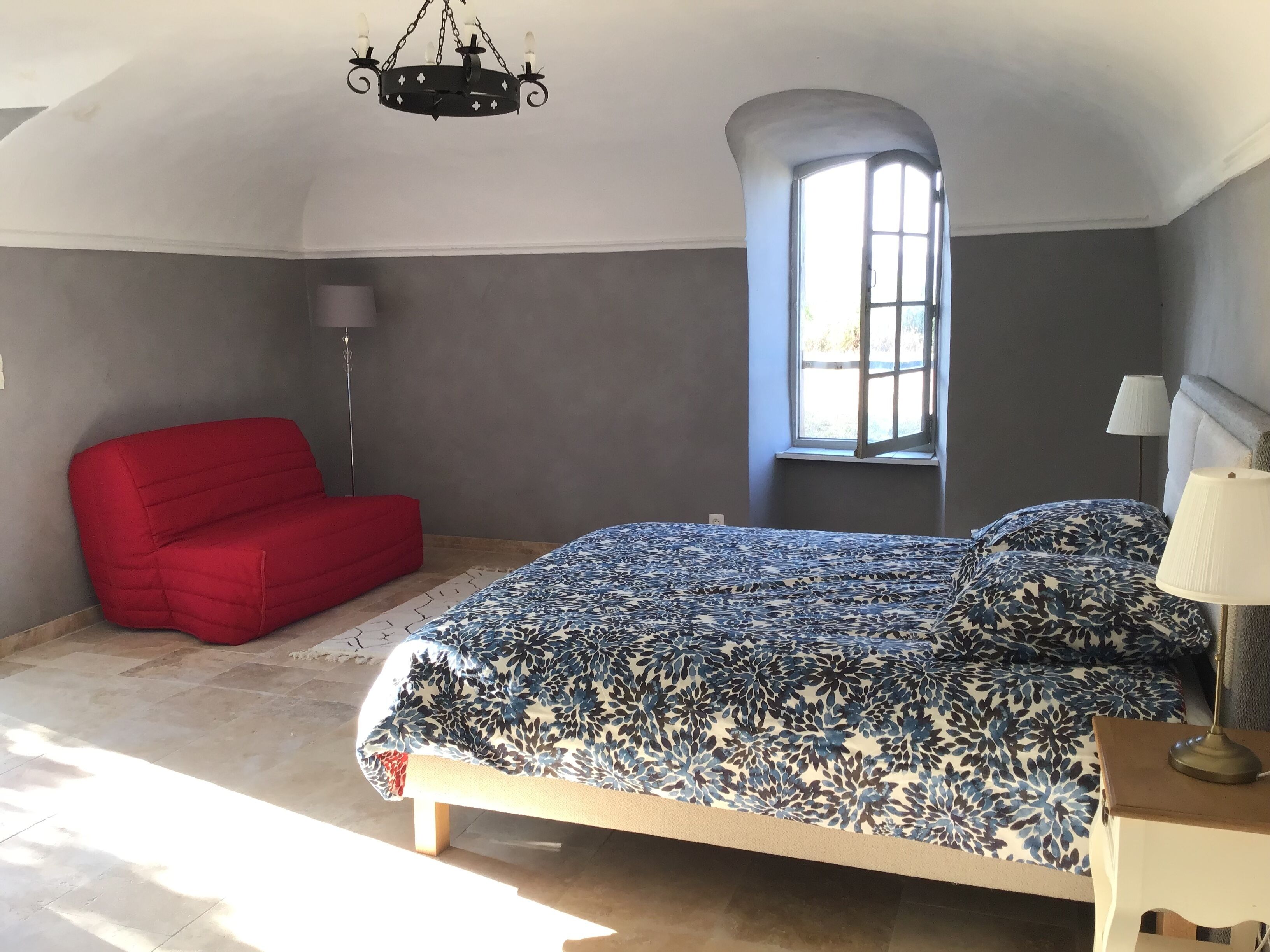 Un dormitorio con una cama, una silla roja, una lámpara de pie y una ventana.