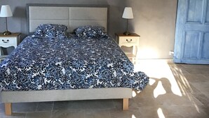 Un dormitorio con una cama, dos mesitas de noche, una mesita auxiliar, una puerta azul y una araña.