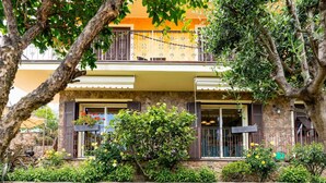 A two-story building with a stone facade, a balcony with metal railings, and a variety of flowering plants in the foreground. - Nice apartment in villa for 5 people with A/C, WIFI, pool, terrace and pets allowed (Borghetto Santo Spirito)