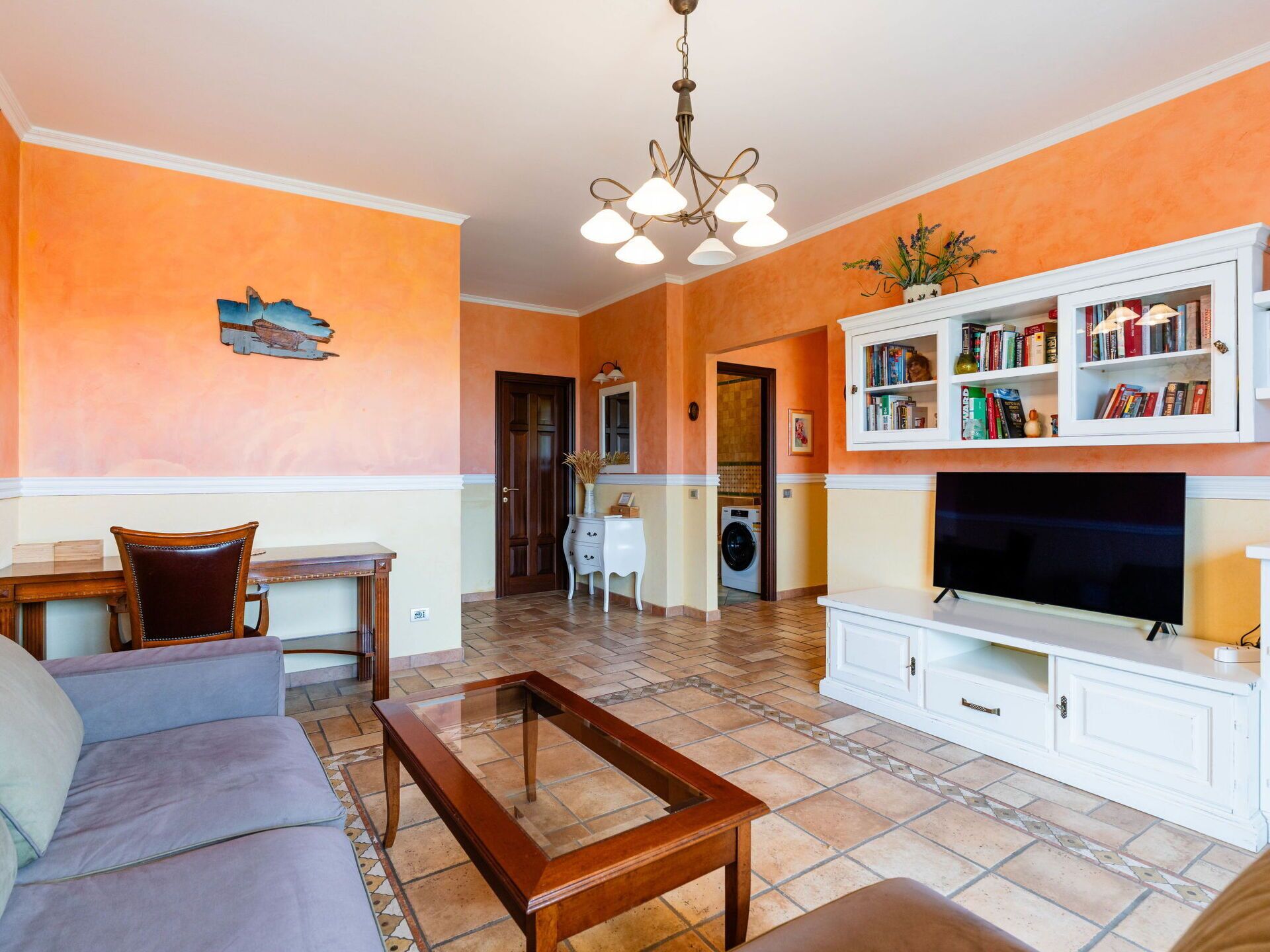A living room with a sofa, coffee table, TV, bookshelf, and a washing machine in the background.