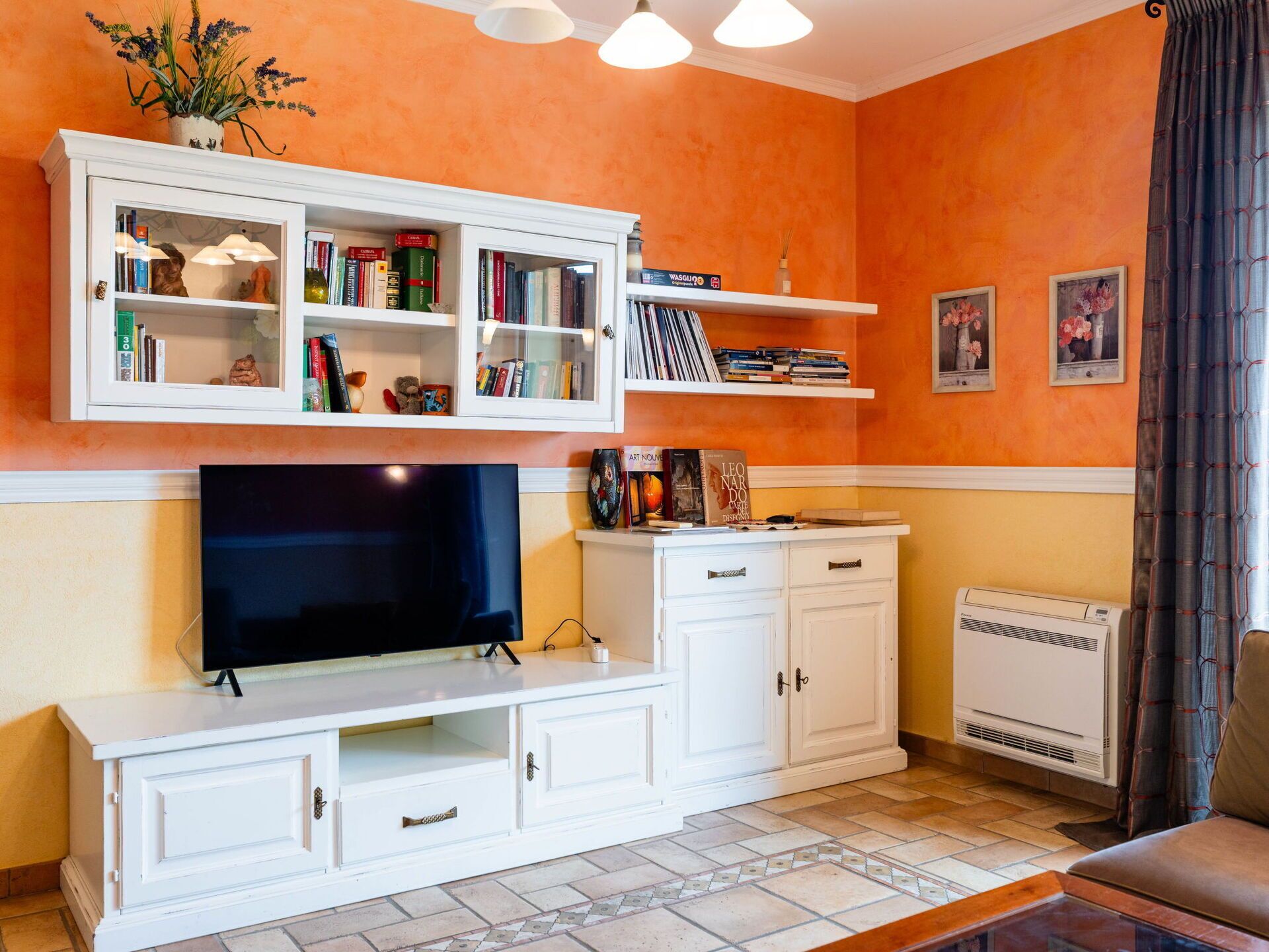 A living room with a TV, white cabinets, and shelves with books and decorative items.