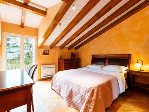 A bedroom with a wooden ceiling, a bed with a quilted blanket, a bedside table with a lamp, and a window with a view of the outside. - Nice apartment in villa for 5 guests with A/C, pool, WIFI, balcony and pets allowed (Borghetto Santo Spirito)