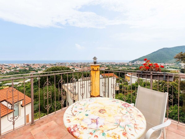 A balcony with a round table and chair, overlooking a cityscape with buildings and a hill. - Nice apartment in villa for 5 guests with A/C, pool, WIFI, balcony and pets allowed (Borghetto Santo Spirito)