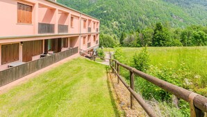A multi-story building with a flat roof, wooden balconies, and a view of a lush green valley and mountains. - Nice apartment for 6 guests with WIFI, TV, patio and panoramic view (Mezzana)