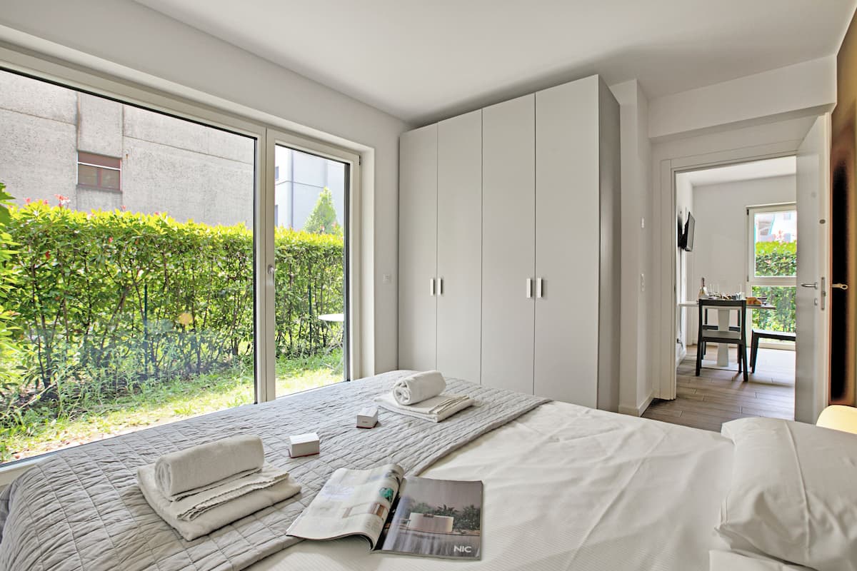A modern bedroom with a large bed, a view of greenery outside, and a door leading to a balcony.