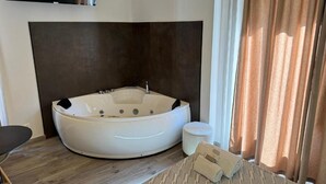 Un baño moderno con una bañera independiente grande, un televisor de pantalla plana en la pared y una ventana con cortinas.