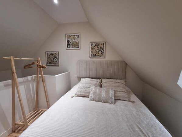 Ein Schlafzimmer mit Schräge, einem Bett mit weißer Bettwäsche und zwei gerahmten Kunstwerken an der Wand.